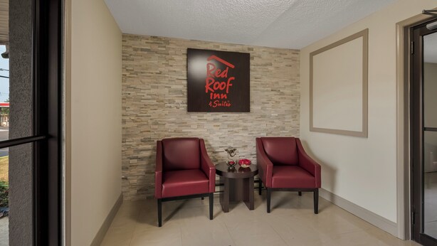 A Red Roof Inn reception area with two red leather chairs, a small table with a vase, and a stone-patterned wall. - Red Roof Inn & Suites Vineland - Buena (Buena)