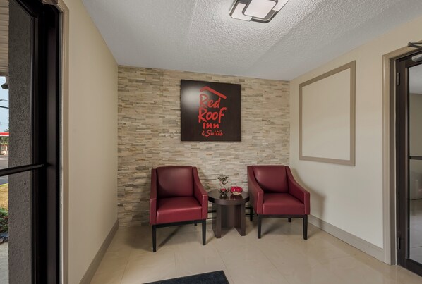 A Red Roof Inn reception area with two red leather chairs, a small table with a vase, and a stone-patterned wall. - Red Roof Inn & Suites Vineland - Buena (Buena)