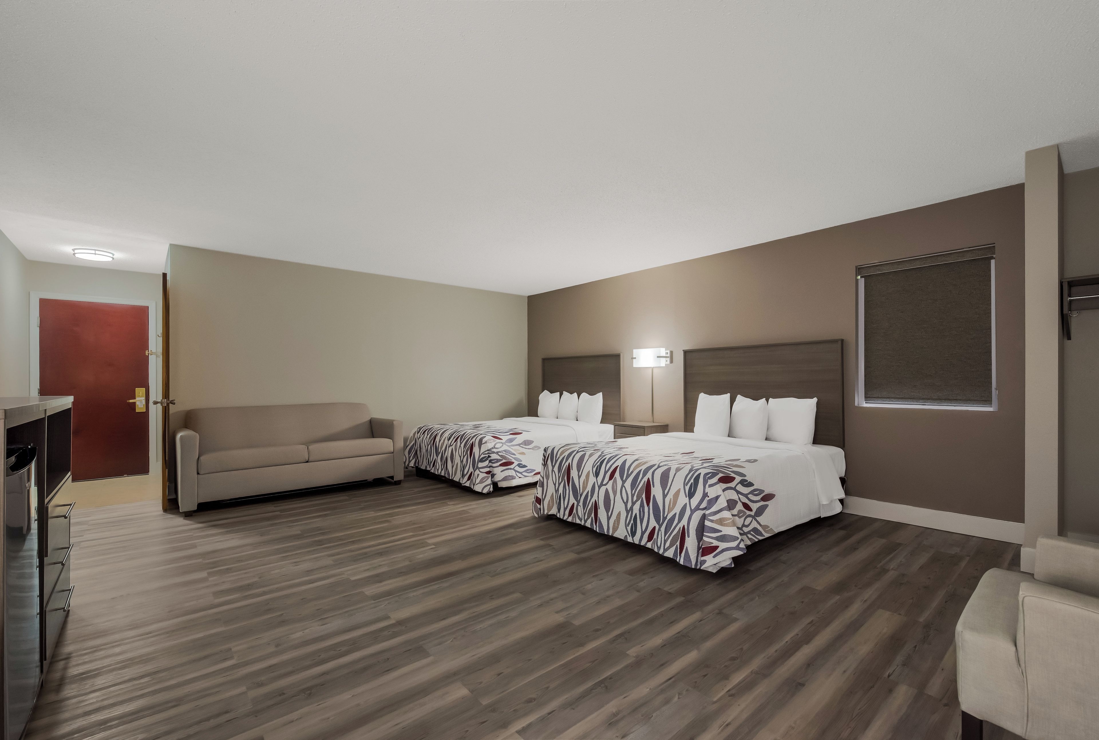 A hotel room with two beds, a sofa, a desk, and a window.