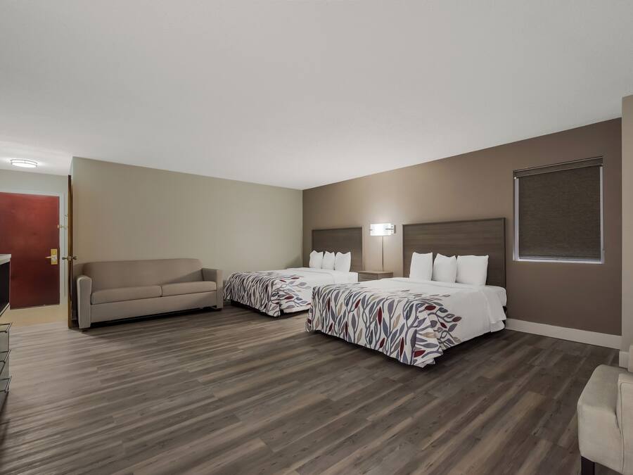 A hotel room with two beds, a sofa, a desk, and a window.