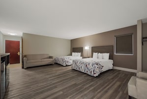Una habitación de hotel con dos camas, un sofá, un escritorio y una ventana.