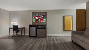 A modern living room with a flat-screen TV mounted on the wall, a wooden cabinet with a microwave, a refrigerator, and a sofa. - Red Roof Inn & Suites Vineland - Buena (Buena)