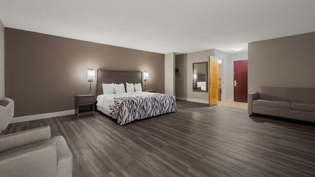 A hotel room with a bed, bedside tables, a nightstand, a sofa, a mirror, and a door. - Red Roof Inn & Suites Vineland - Buena (Buena)