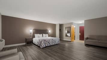A hotel room with a bed, bedside tables, a nightstand, a sofa, a mirror, and a door.
