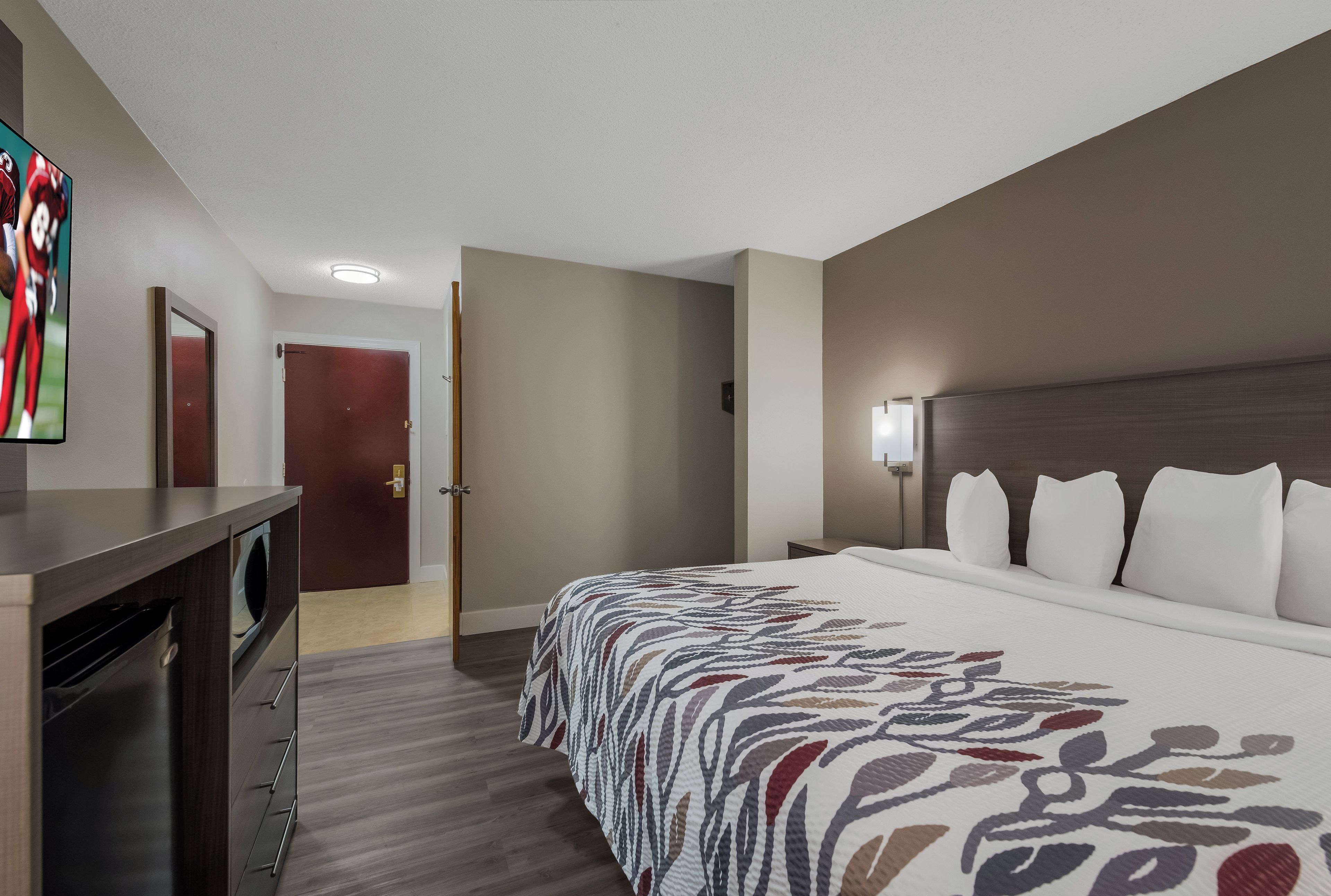 A hotel room with a bed, a desk, a television, and a door.