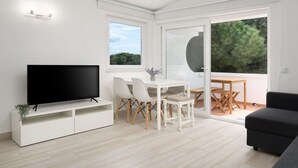 Ein modernes Wohnzimmer mit Fernseher, Esstisch mit Stühlen und einer Couch.