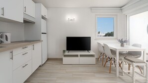 Eine moderne Küche mit weißen Schränken, einem Flachbildfernseher und einem Essbereich mit weißem Tisch und Stühlen.