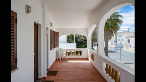 A balcony with a view of a street and palm trees, a white chair, and a door with shutters. - Bright Albufeira - 5min to the beach by LovelyStay (Albufeira)