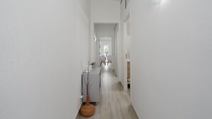 A narrow hallway with white walls and wooden flooring, leading to a room with a large window and a chair. - Bright Albufeira - 5min to the beach by LovelyStay (Albufeira)