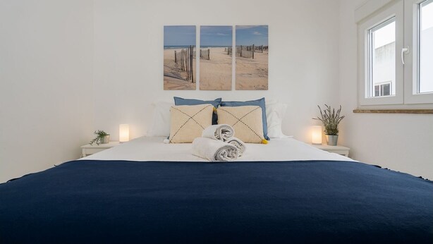 A bedroom with a large bed, a window, and three wall-mounted pictures of a beach scene. - Bright Albufeira - 5min to the beach by LovelyStay (Albufeira)