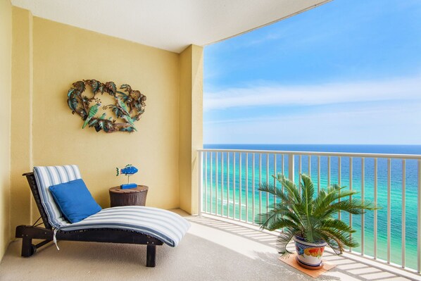 Enjoy the ocean view from this balcony with a lounge chair, side table, and potted plant.