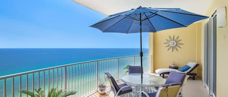 A balcony with a table and chairs, a blue umbrella, and a view of the ocean.