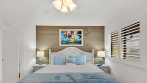 A bedroom with a large bed, wooden headboard, two bedside tables with lamps, a painting above the bed, and a window with blinds. - ⭐Sandprints A12-350yds 2 Beach-2BR ⭐ (Miramar Beach)