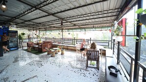 Un espacio al aire libre techado con suelo de baldosas, mobiliario de mimbre y plantas en macetas.