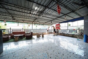 An indoor space with a tiled floor, seating area with wicker furniture, and a large window with a view. - MAPLE THE HUBZ-Hostel (Mumbai)