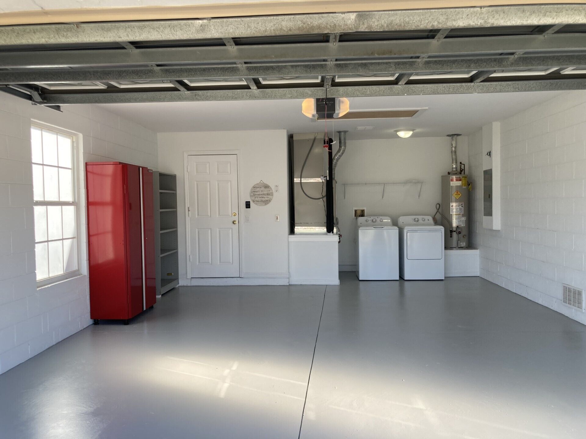 A clean, well-lit laundry room with a white door, a red cabinet, and two white washing machines.