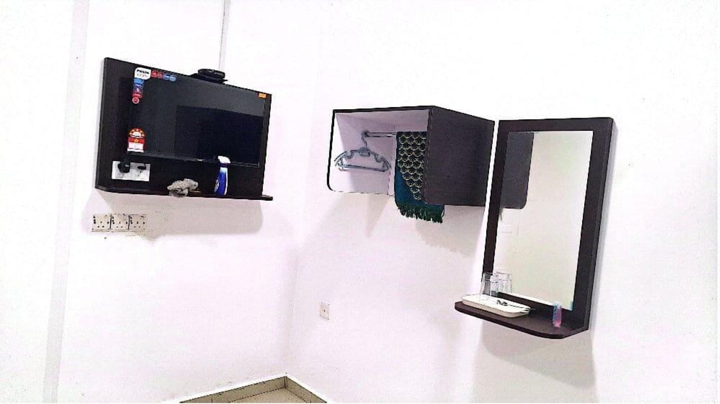 A bathroom with a black shelf holding a hairdryer and a bottle, and a mirror with a stand.