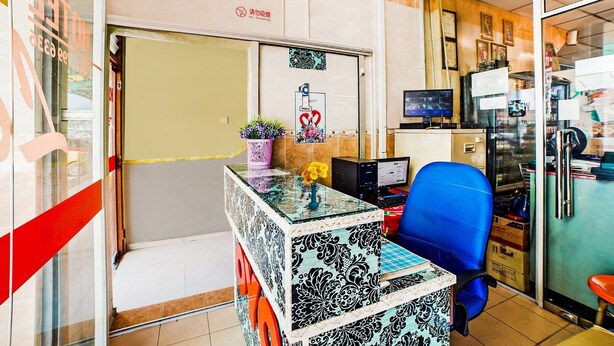 Un mostrador de recepción con una computadora, una silla de oficina azul y una pequeña mesa con un jarrón de flores.