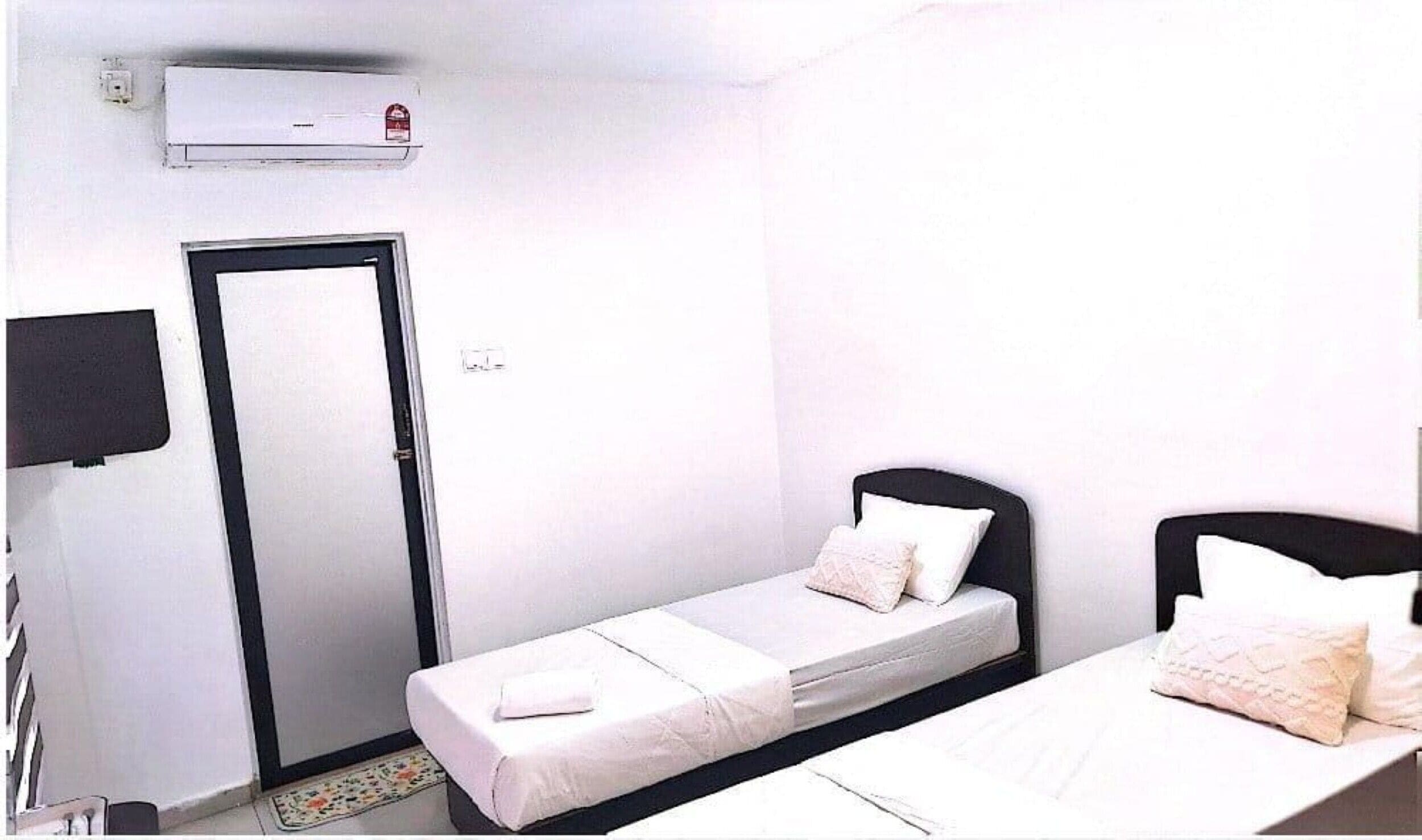 A small, single-bed room with a door, a flat-screen TV, and a window.