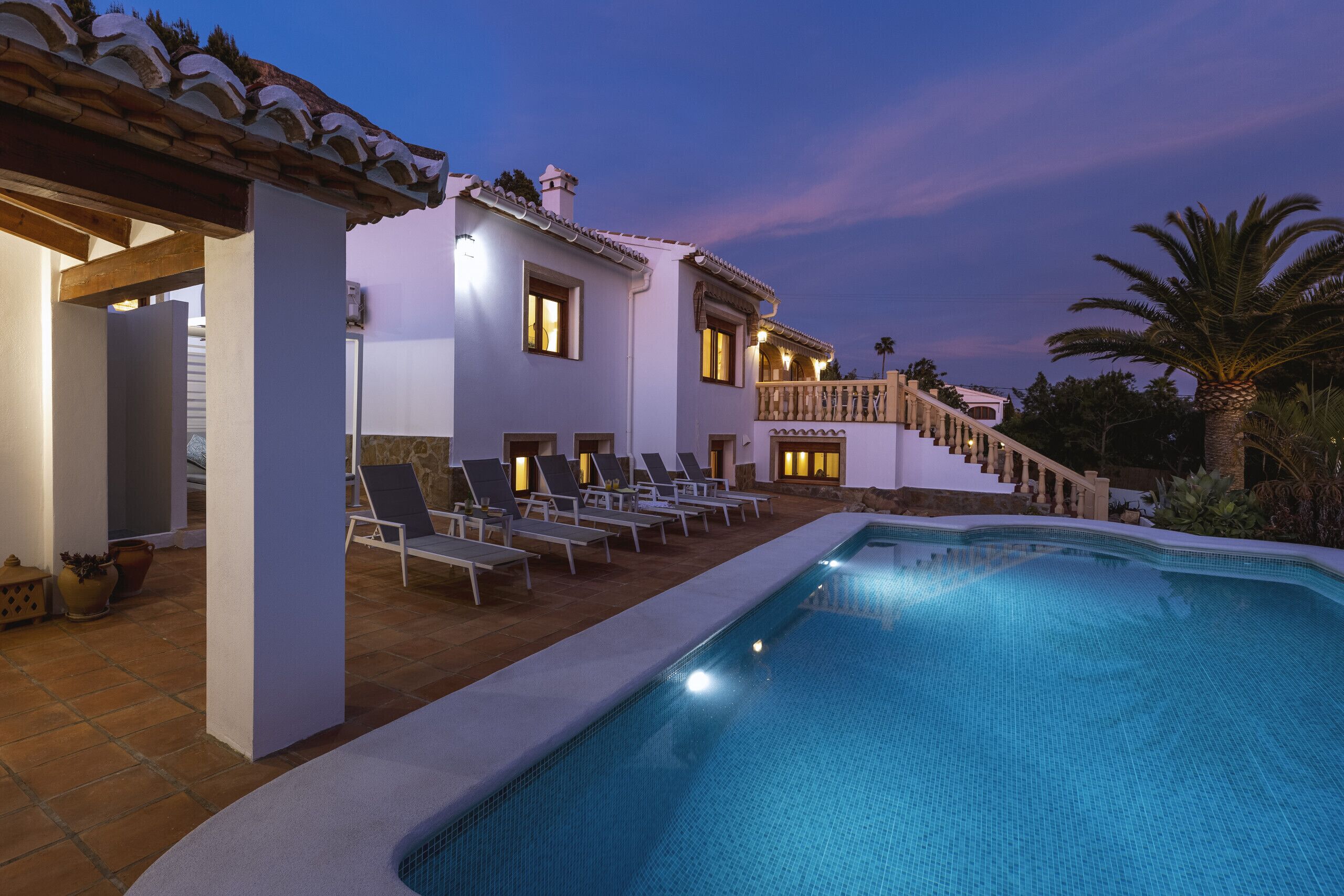 A pool area with lounge chairs and a staircase leading to a second floor.