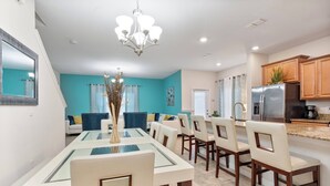 A modern kitchen with a built-in refrigerator, a dining area with a glass-top table, and a living room with a sofa and chairs.