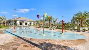 A water feature with multiple jets and colorful structures, surrounded by palm trees and lounge chairs.