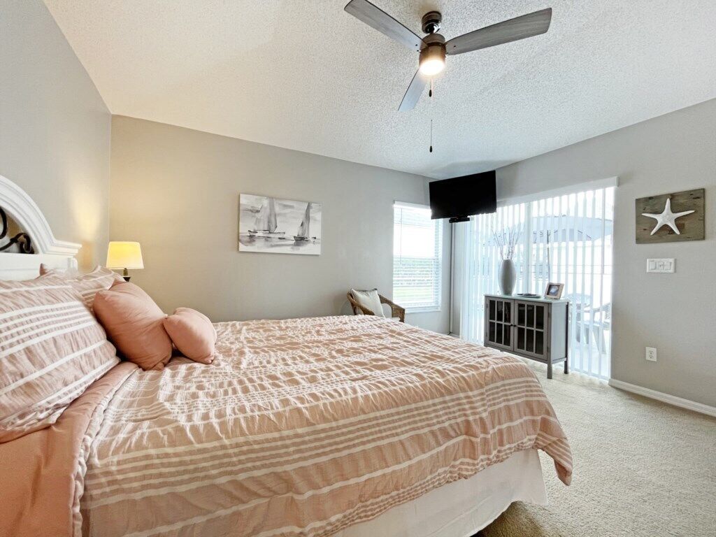 A bedroom with a bed, a ceiling fan, a TV, and a window with blinds.