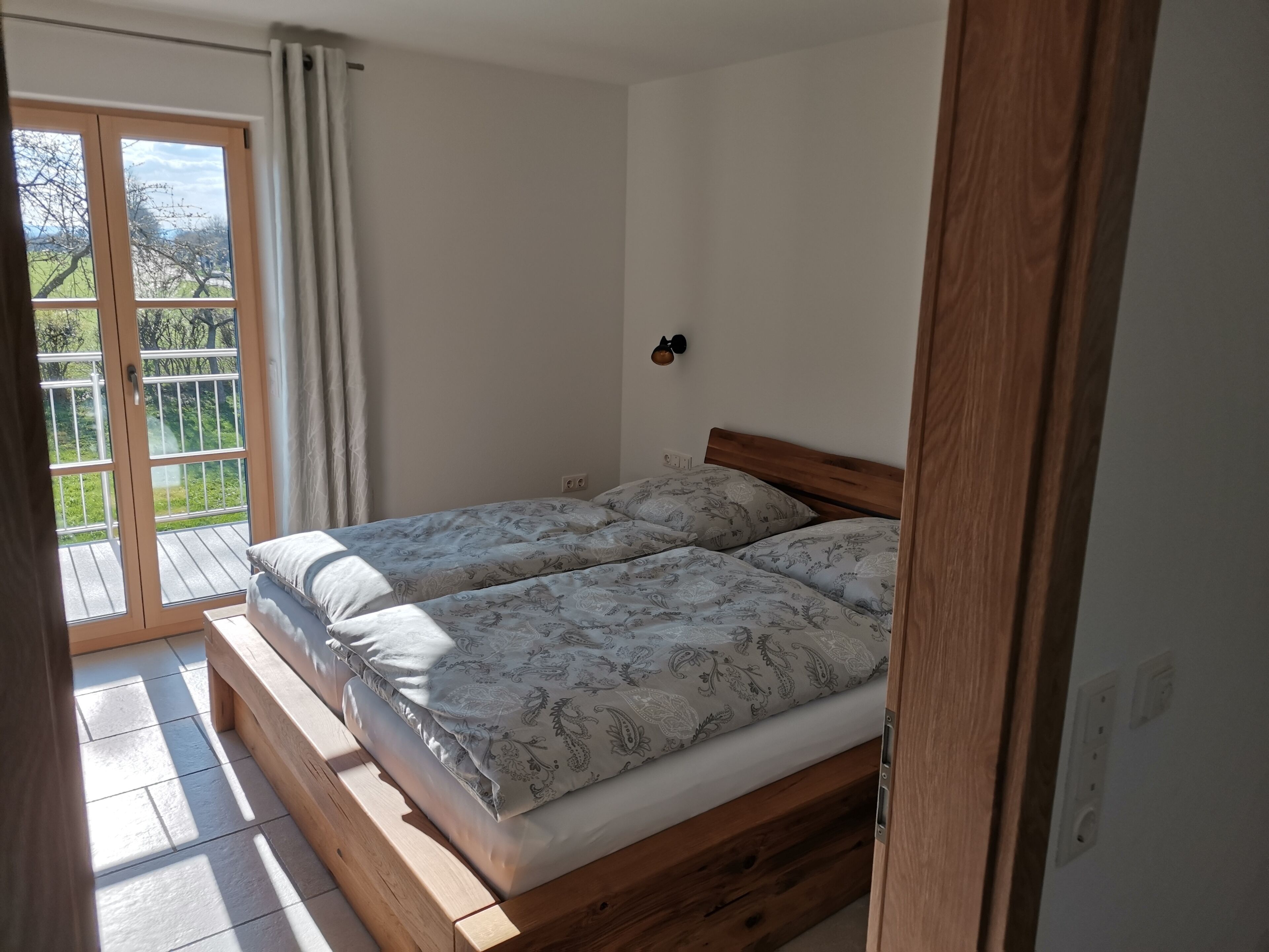 Ein Schlafzimmer mit einem hölzernen Bett, einer Schiebetür zum Balkon und einer kleinen Wandleuchte.