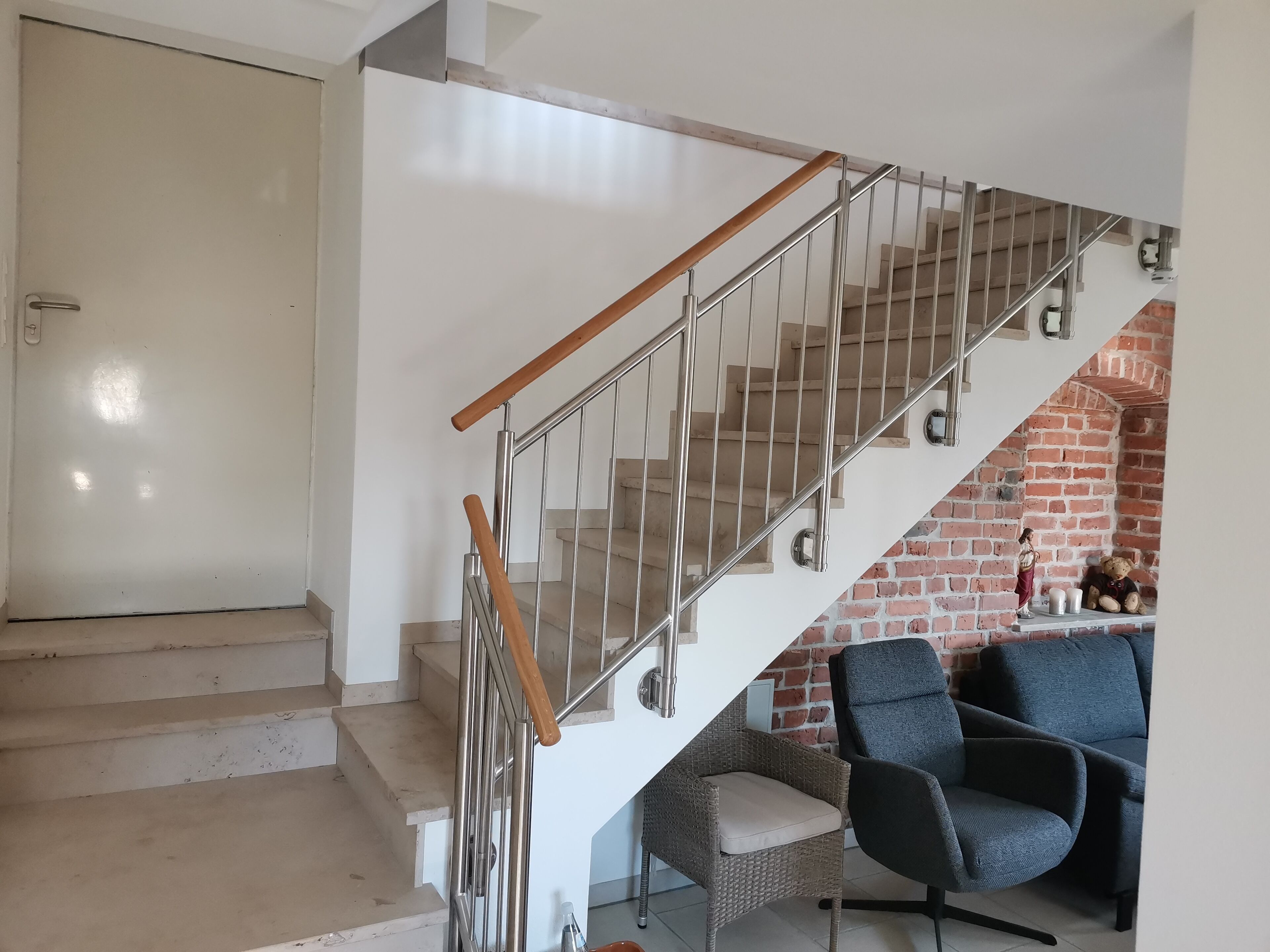 A staircase with a wooden handrail and metal balusters, leading to a brick wall.