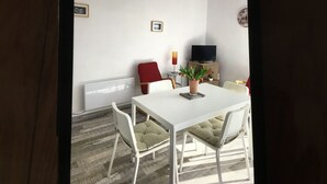 Ein Essbereich mit einem weißen Tisch und Stühlen, einem roten Sessel, einer Zimmerpflanze, einem Fernseher und einer Heizung.