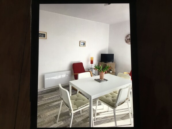 A dining area with a white table and chairs, a red chair, a potted plant, a television, and a radiator.