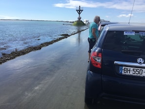 A car parked near a body of water with a rocky shore and a lighthouse in the background.