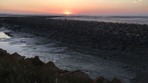 Ein Küsten-Sonnenuntergang mit einem steinernen Wellenbrecher und ruhiger See.