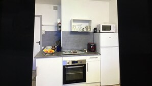 Eine kompakte Küche mit weißen Schränken, einer Mikrowelle, einer Kaffeemaschine und einem kleinen Backofen.