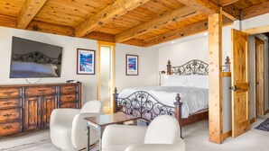 Un dormitorio con techo de madera, una cama con cabecera de metal, un aparador, un televisor y una silla.