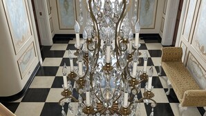 A grand staircase with a black and white checkered floor, a chandelier with crystal decorations, and a patterned bench. - 13,000 sq. ft. 6BR Estate on 5 acres Swim Spa, Hot Tub, Pool Table, Game Room (Muncie)
