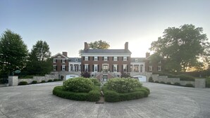 A large, symmetrical building with a central statue, surrounded by well-manicured bushes and a paved courtyard. - 13,000 sq. ft. 6BR Estate on 5 acres Swim Spa, Hot Tub, Pool Table, Game Room (Muncie)