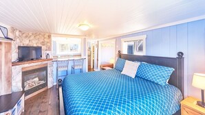 A bedroom with a large bed, a fireplace, a television, and a small kitchen area.