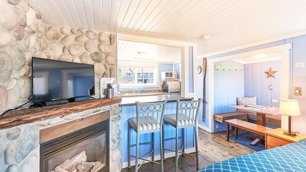 A cozy room with a stone wall, a flat-screen TV, a fireplace, a bar area with stools, and a dining table with a lamp.