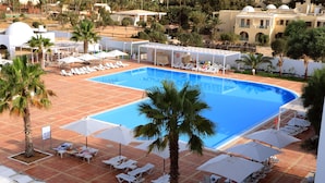 Una piscina con sillas de descanso blancas y sombrillas, rodeada de palmeras y edificios.