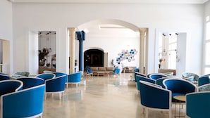 Un vestíbulo amplio con sillas azules dispuestas en filas, un área de estar central con un sofá y una mesita de café, y decoración en las paredes.