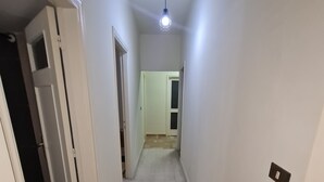 Un pasillo estrecho con paredes blancas y piso de baldosas, que conduce a una puerta al final.