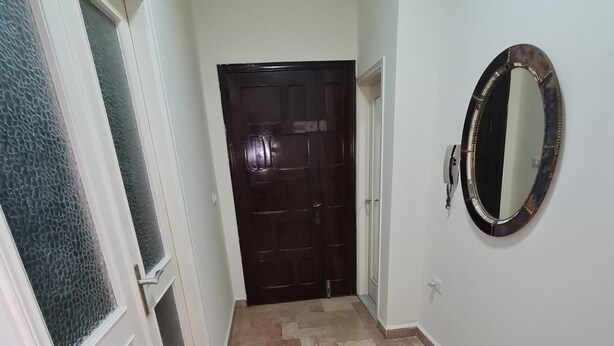 Un pasillo con suelo de baldosas, una puerta de madera oscura y un espejo fijado a la pared.