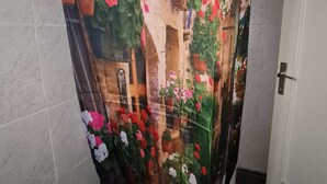Baño con cortina de ducha que muestra un jardín con macetas y flores.