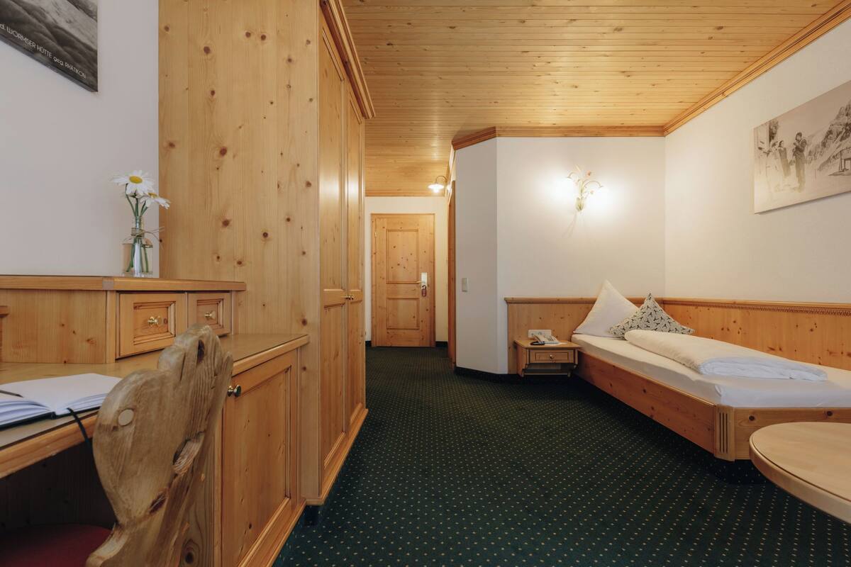A wooden room with a bed, a desk, and a chair. There is a vase with flowers on the desk.