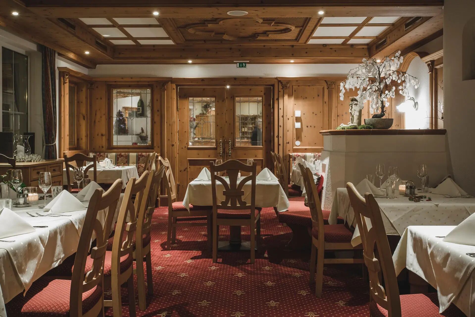 Een restaurant met houten inrichting, meerdere eettafels en een kroonluchter.