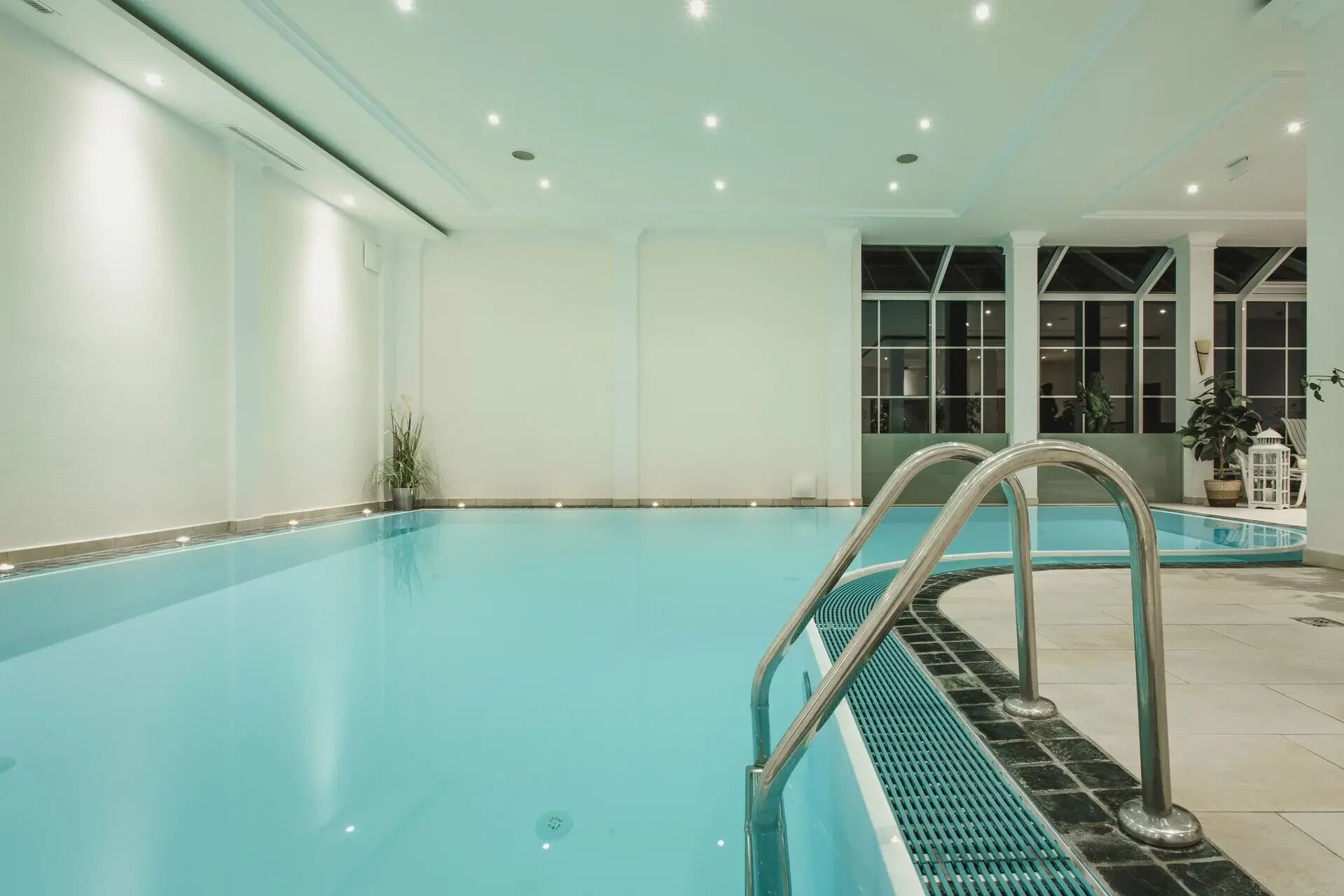 A large indoor swimming pool with clear blue water, a metal ladder, and a tiled floor.