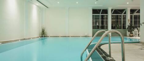 A large indoor swimming pool with clear blue water, a metal ladder, and a tiled floor.