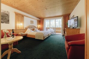 A hotel room with a bed, a television, a dining table, and a balcony with a view of the mountains. - Hotel Hirschen (Silbertal)