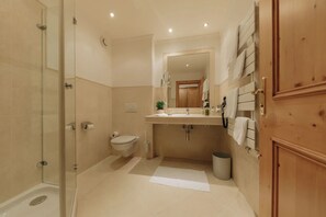 A bathroom with a glass shower enclosure, a toilet, a sink with a mirror, and a towel rack. - Hotel Hirschen (Silbertal)